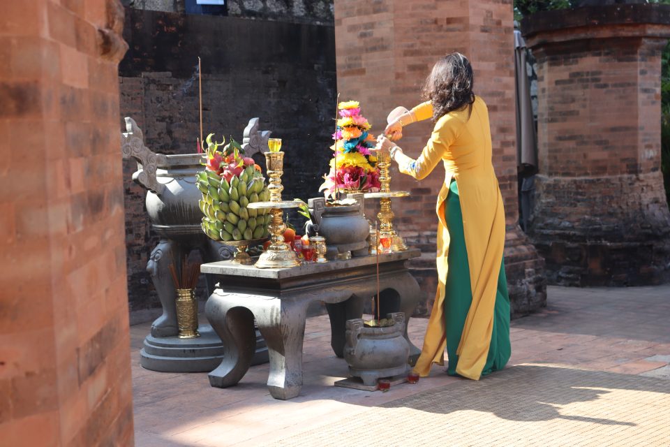 Ragazza vietnamita vestita di giallo che accende incensi in un tempio Vietnamita.